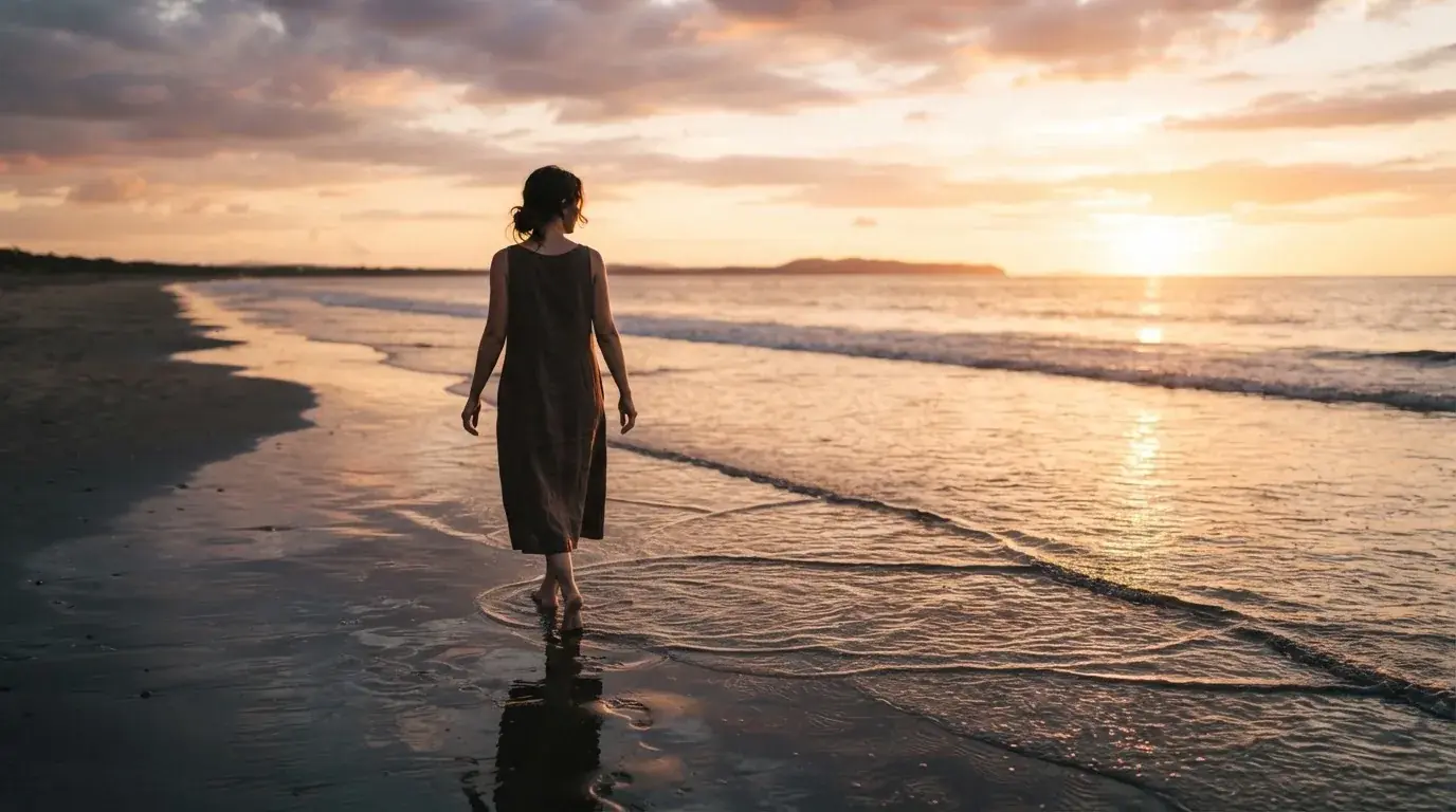 Persona caminando por la orilla del mar al atardecer en actitud relajada.