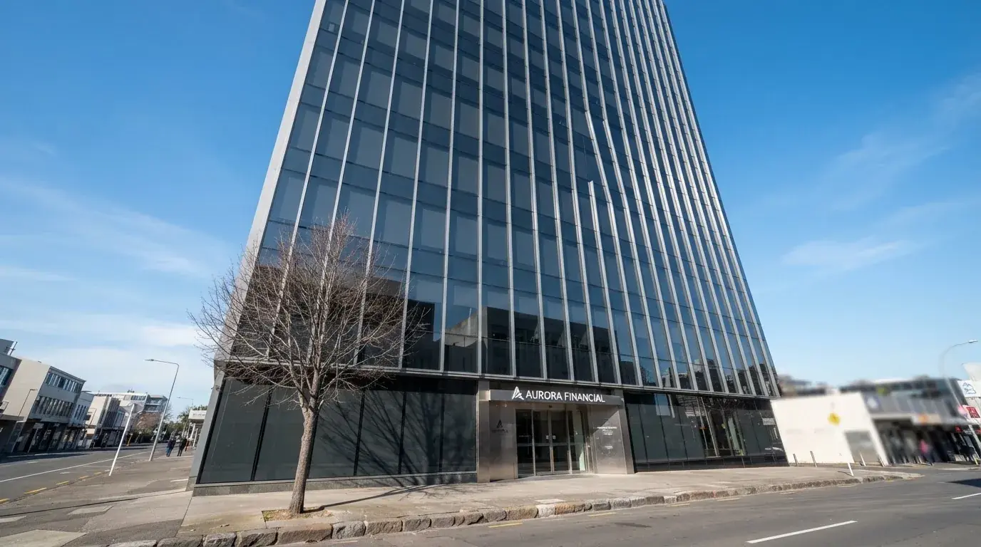 Un edificio de oficinas moderno con cristales reflectantes bajo un cielo despejado, visto desde una calle tranquila.