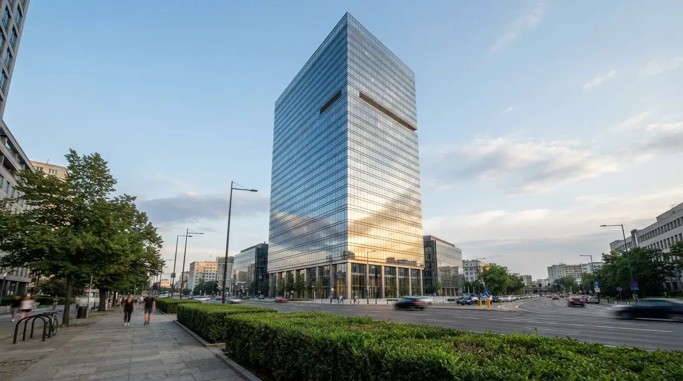 Un edificio de oficinas con fachada de cristal reflejando el cielo, fotografiado desde la acera de una calle ancha.
